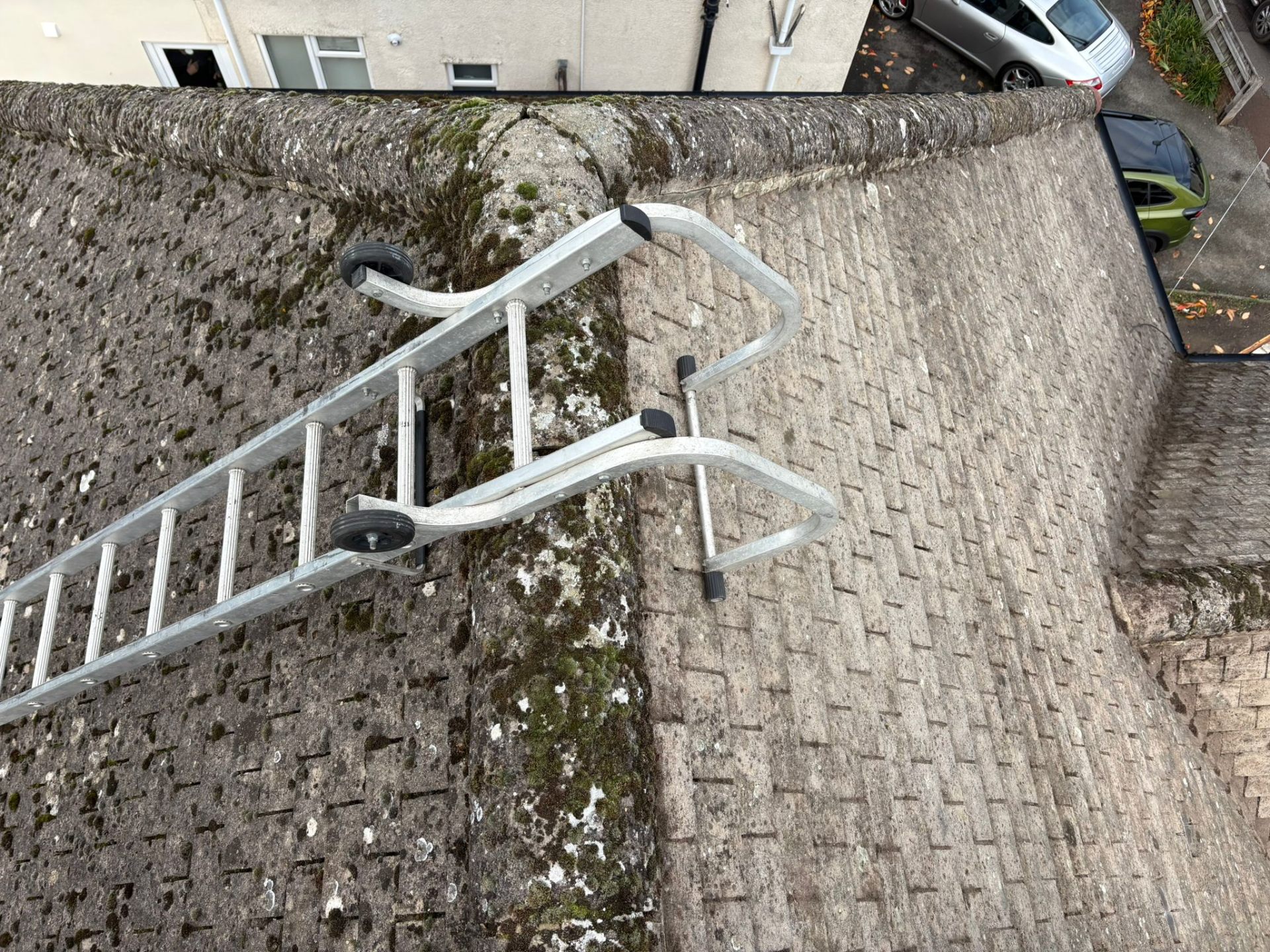 Roof ladder secured on a moss-covered stone roof ready for inspection and cleaning